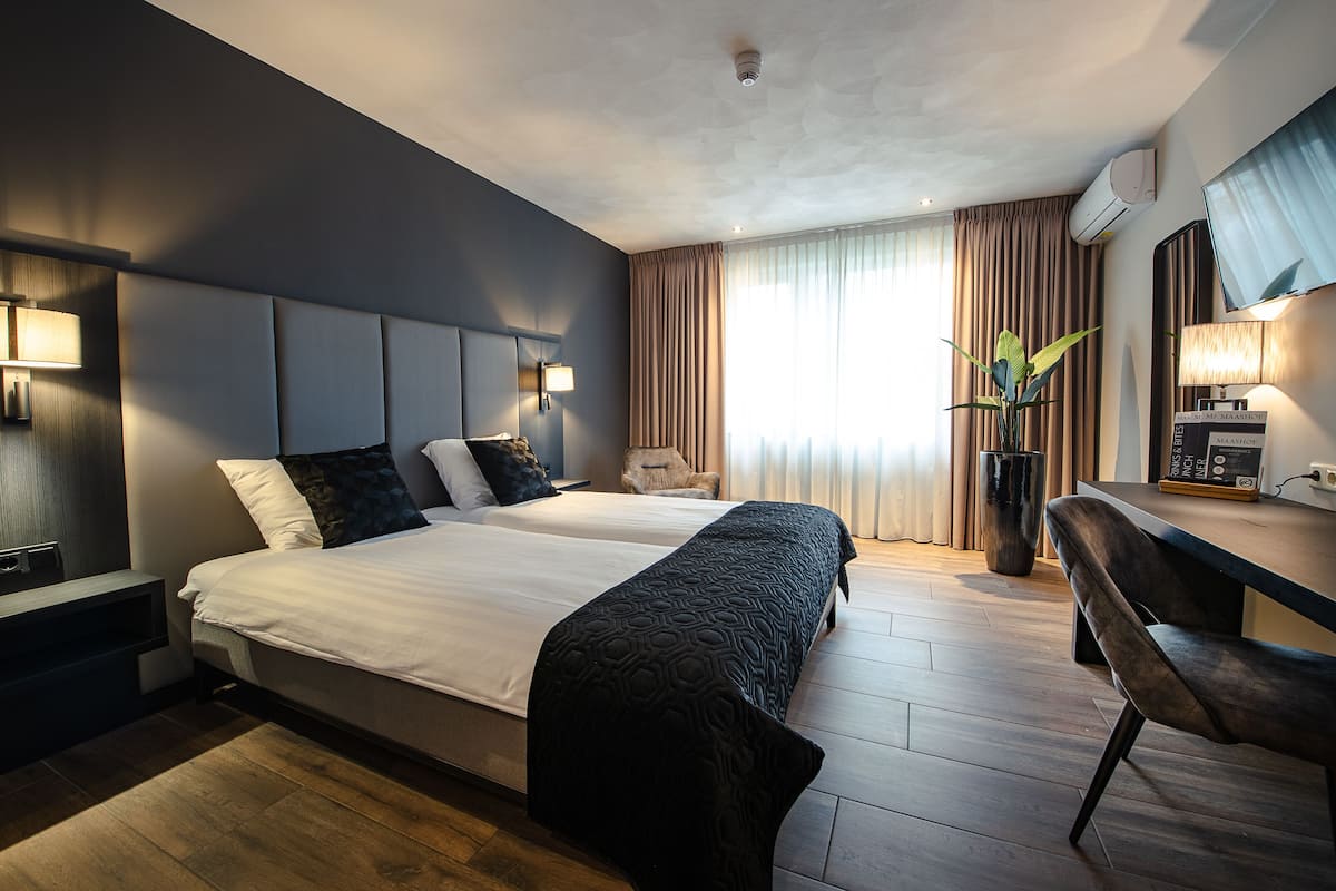 Une chambre d’hôtel avec un grand lit, un bureau, une chaise, une plante et un téléviseur.