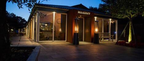 A restaurant named 'MAASHOF' with a brick facade, large windows, and outdoor seating area.