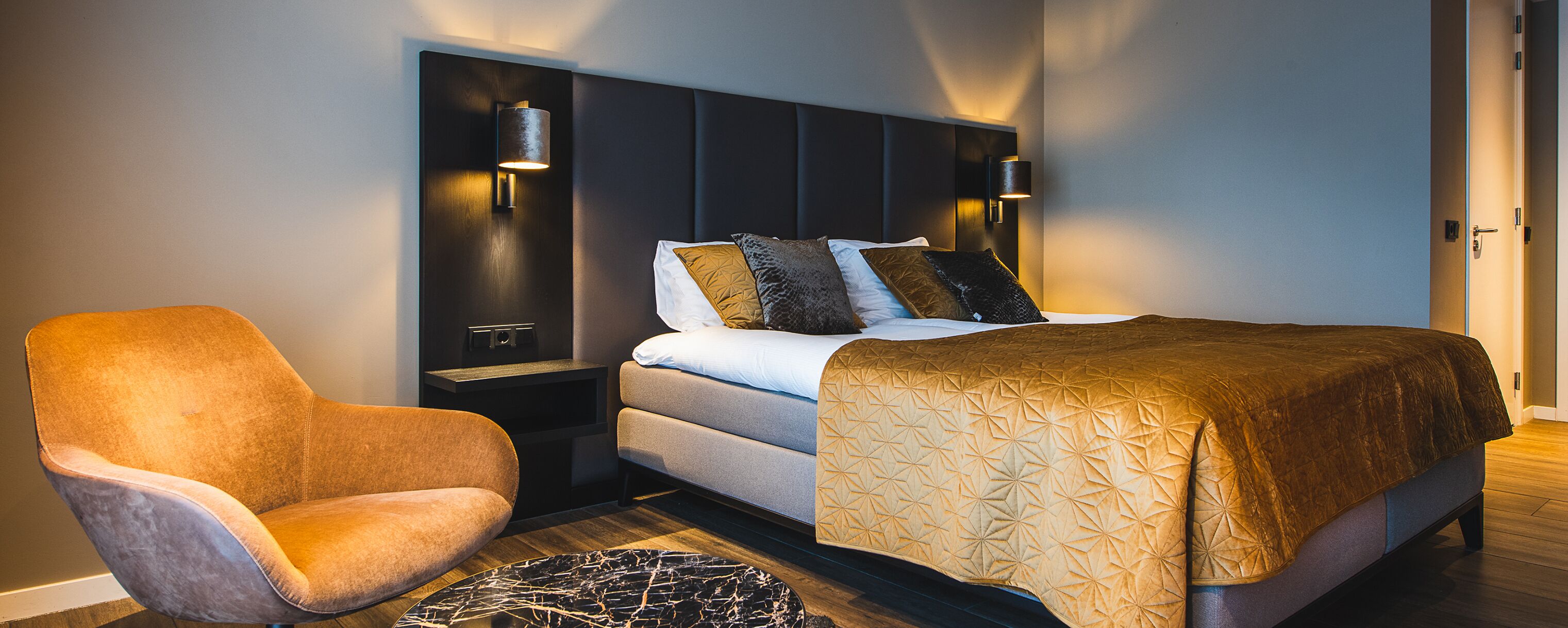 A modern hotel room with a bed, a chair, and wall-mounted lights.