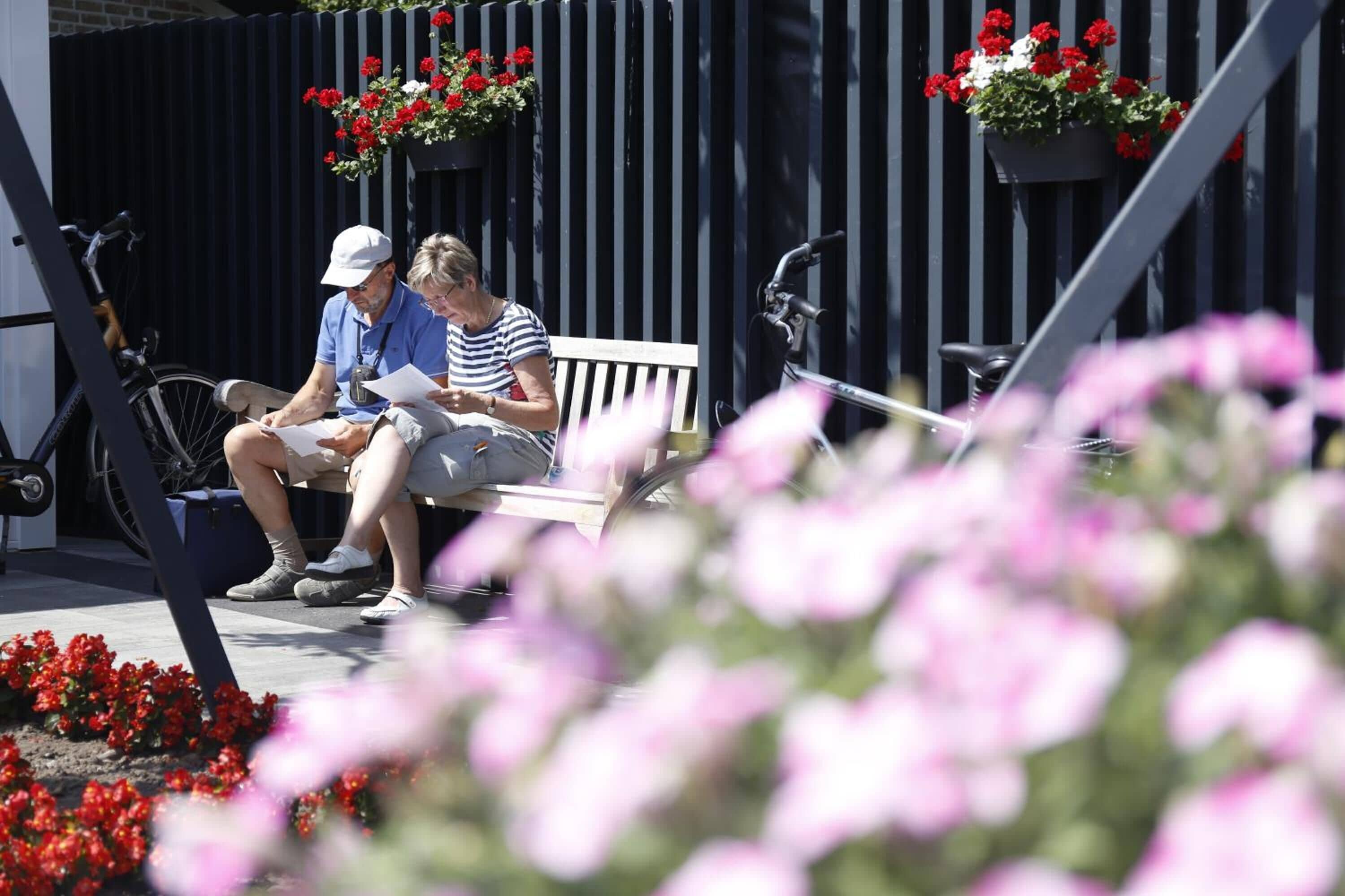 A bench with two people sitting, a bicycle, and flower planters.