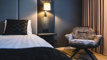 Ein modernes Hotelzimmer mit Bett, Sessel, Nachttisch und Wandlampe.