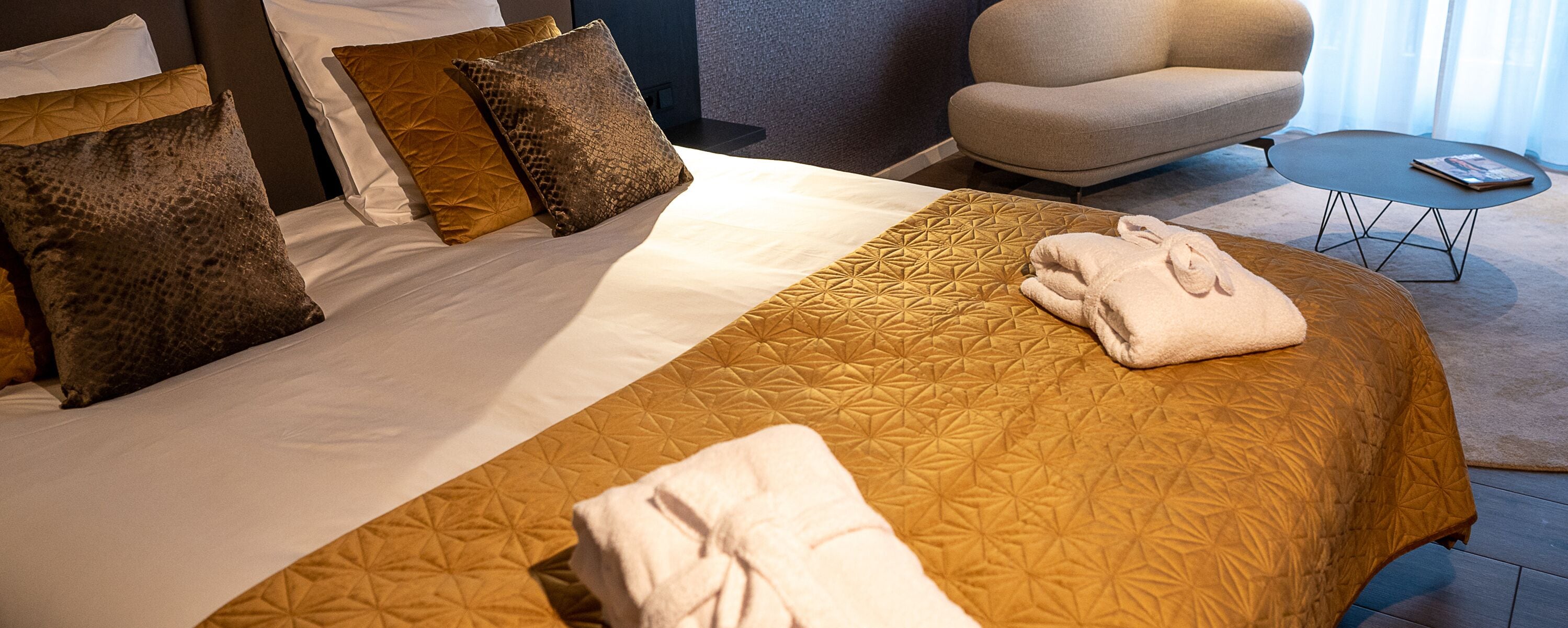 Een net opgemaakt bed met een beddekleed met patroon, twee kussens en een opgevouwen handdoek aan de zijkant.