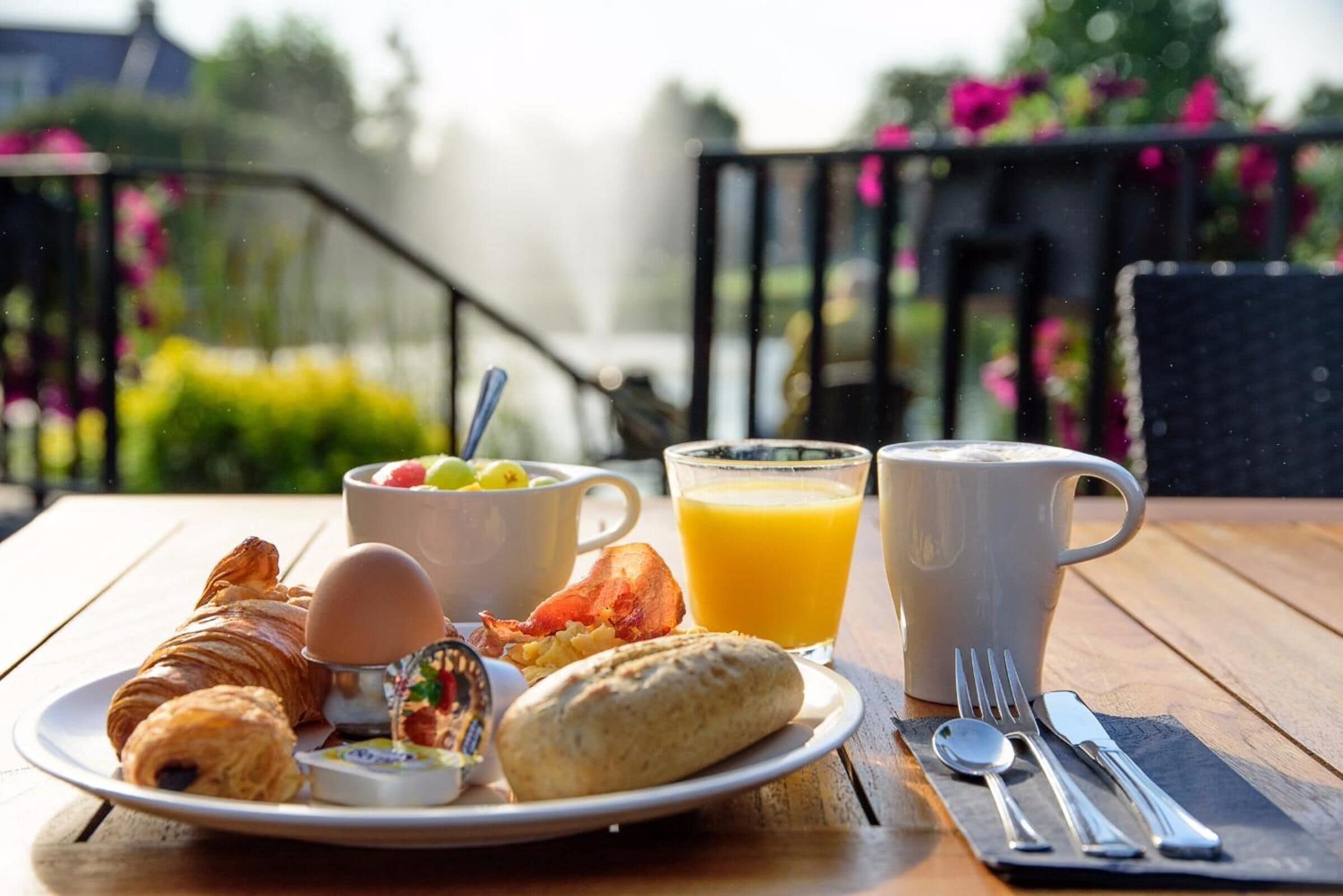 A breakfast table with croissants, eggs, a muffin, a bowl of fruit, a glass of orange juice, and a cup of coffee.