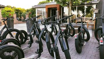 A row of electric bicycles parked outside a building with a sign reading "MAASHOF".