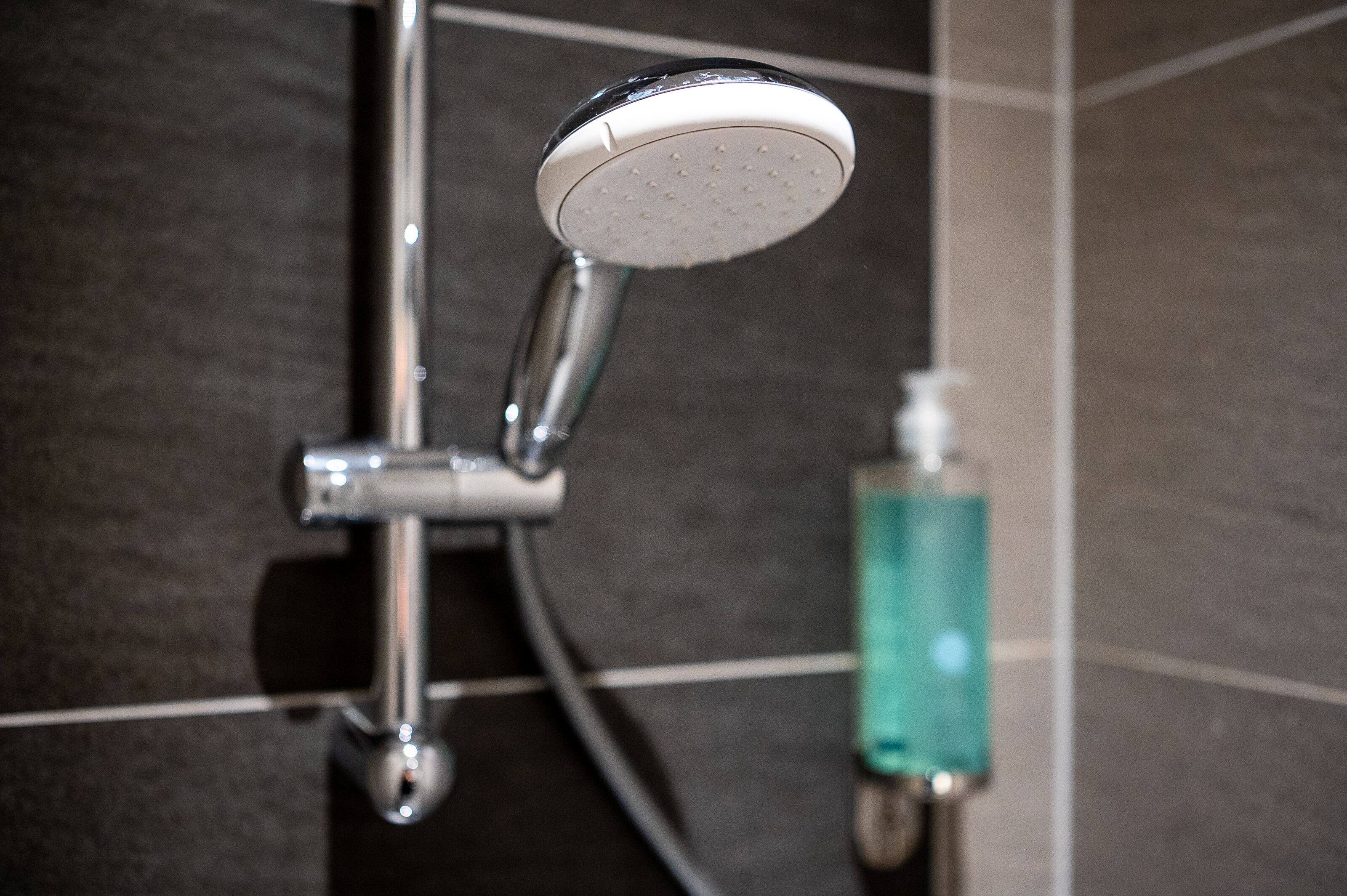 A showerhead with a handheld attachment, a soap dispenser, and a tiled wall.