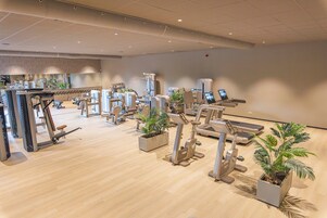 A modern fitness center with various exercise machines, including treadmills and stationary bikes, and several potted plants.