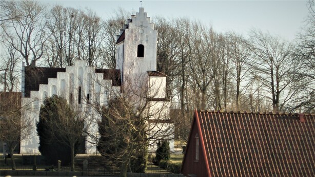 Une structure ressemblant à un château, dotée d’une tour, entourée d’arbres sans feuilles et d’un bâtiment au toit rouge.