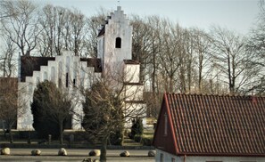A castle-like structure with a tower, surrounded by leafless trees and a red-roofed building. - Hoby Gård Bed & Breakfast (Borrby)