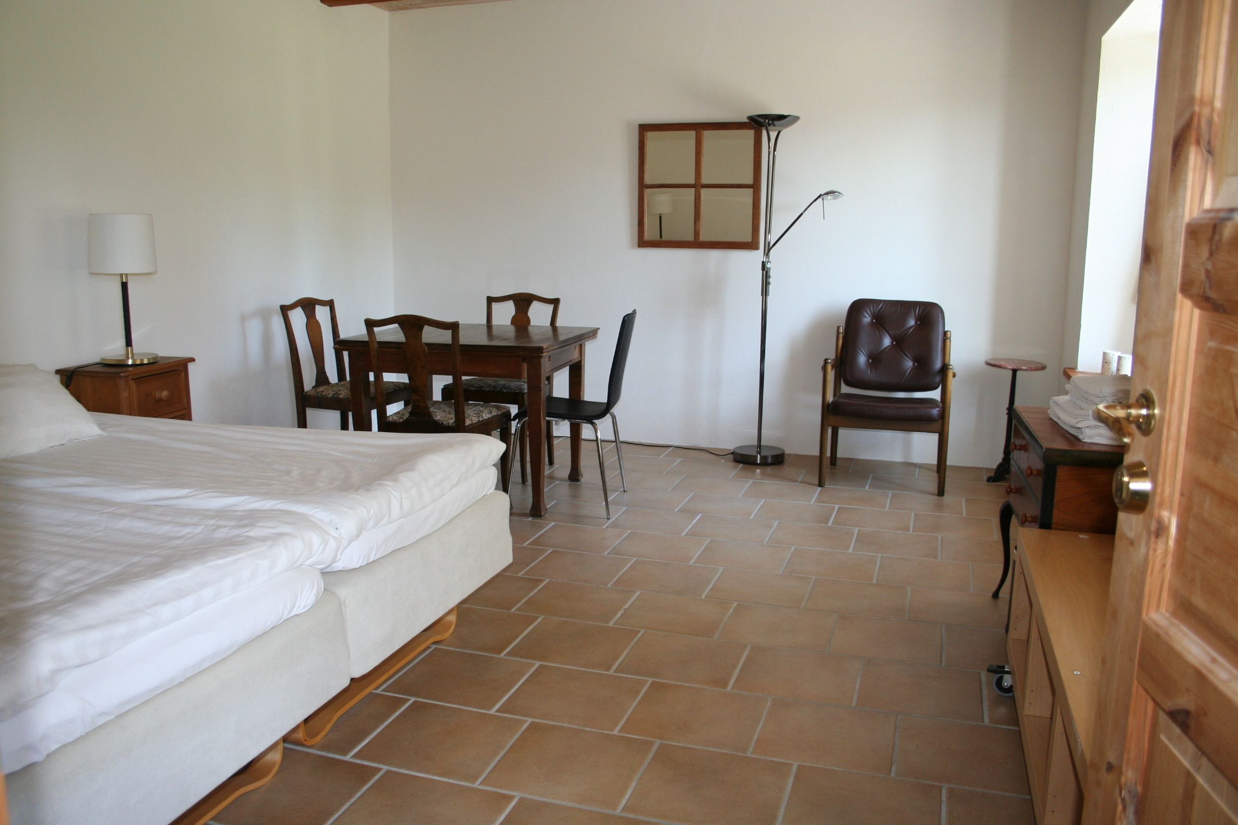 A bedroom with a bed, a desk with a chair, a floor lamp, and a wardrobe.