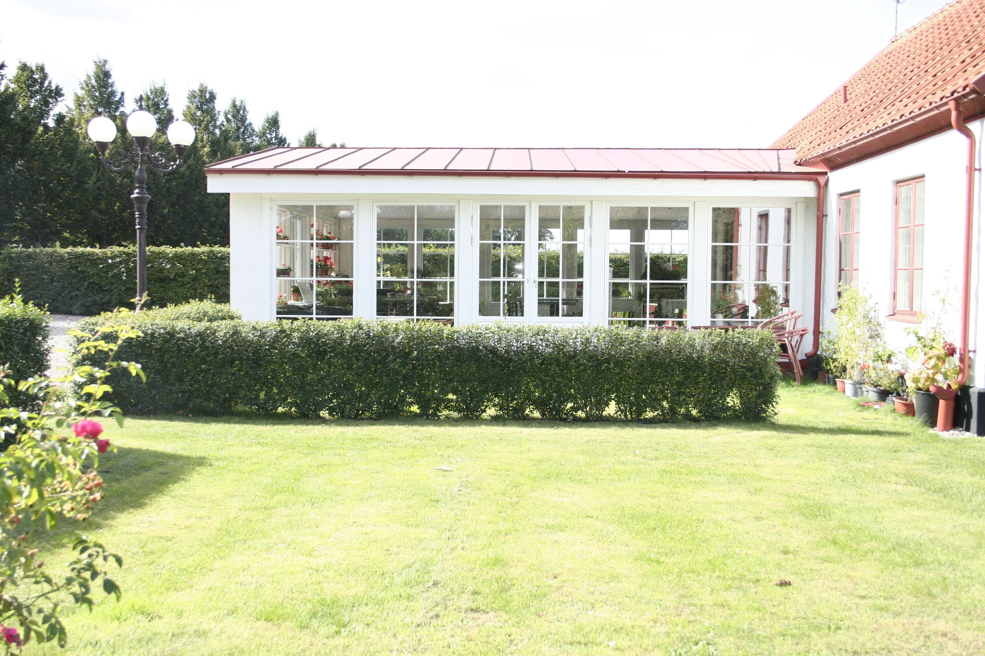 A conservatory with a glass roof, surrounded by a well-maintained lawn and hedges.
