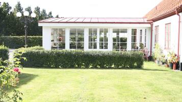 A conservatory with a glass roof, surrounded by a well-maintained lawn and hedges.