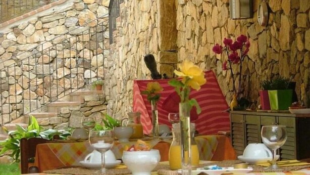 An outdoor dining area with stone walls, a table set with plates, glasses, and flowers. - Casale Coreallo (Spotorno)
