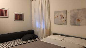 Un dormitorio con una cama, una mesita de noche, un aire acondicionado de pared y dos cuadros enmarcados.