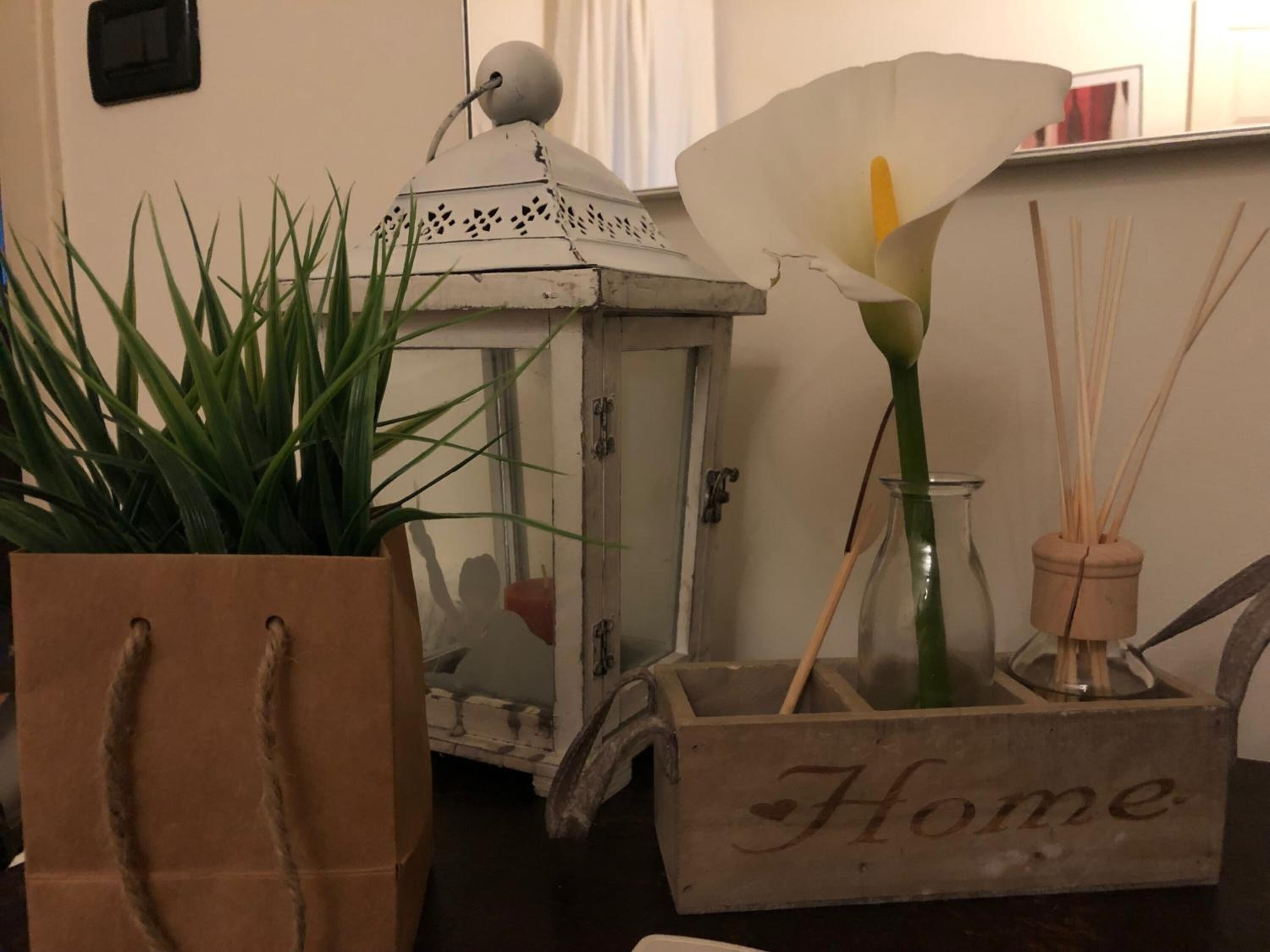 A wooden box with the word "Home" on it, a white lantern, a calla lily, and a potted plant.
