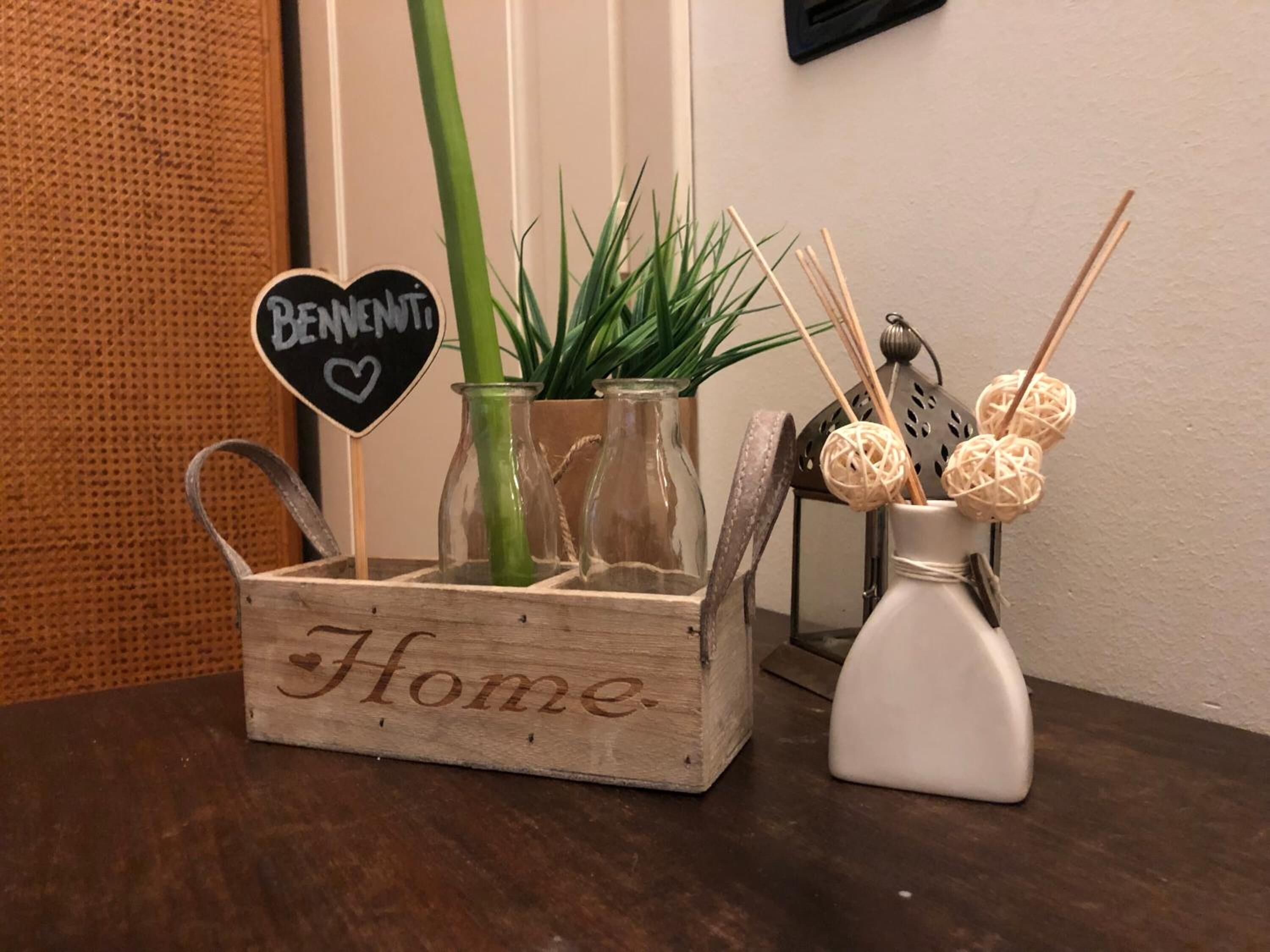 Une boîte en bois étiquetée « Maison », avec des vases en verre, une plante verte et des objets décoratifs placés sur une table.
