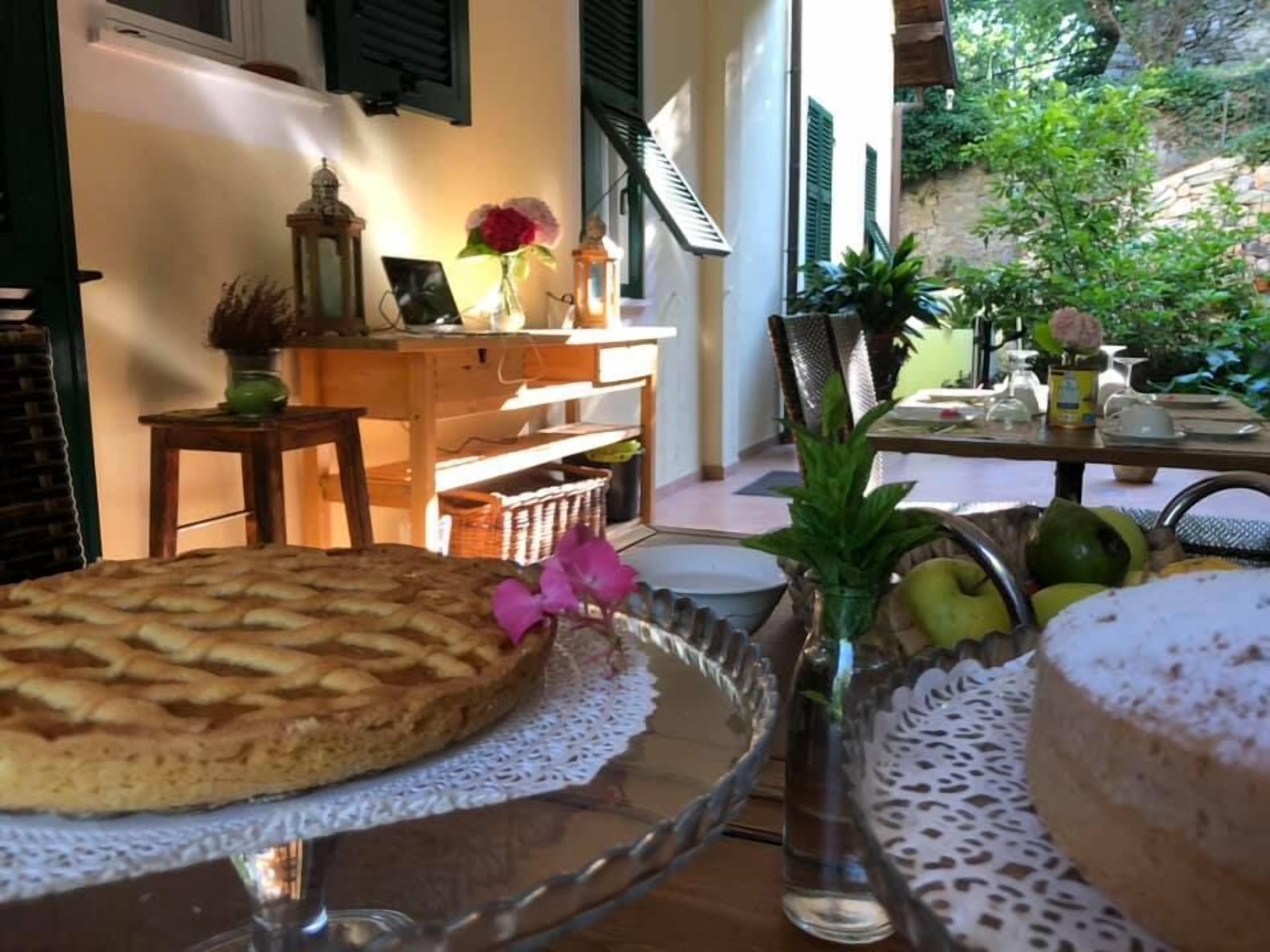 A dining table with a cake, a glass vase with flowers, and a fruit bowl.