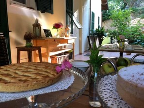 A dining table with a cake, a glass vase with flowers, and a fruit bowl. - Casale Coreallo (Spotorno)