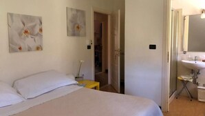 A bedroom with a bed, a nightstand, a mirror, and a bathroom with a sink. - Casale Coreallo (Spotorno)
