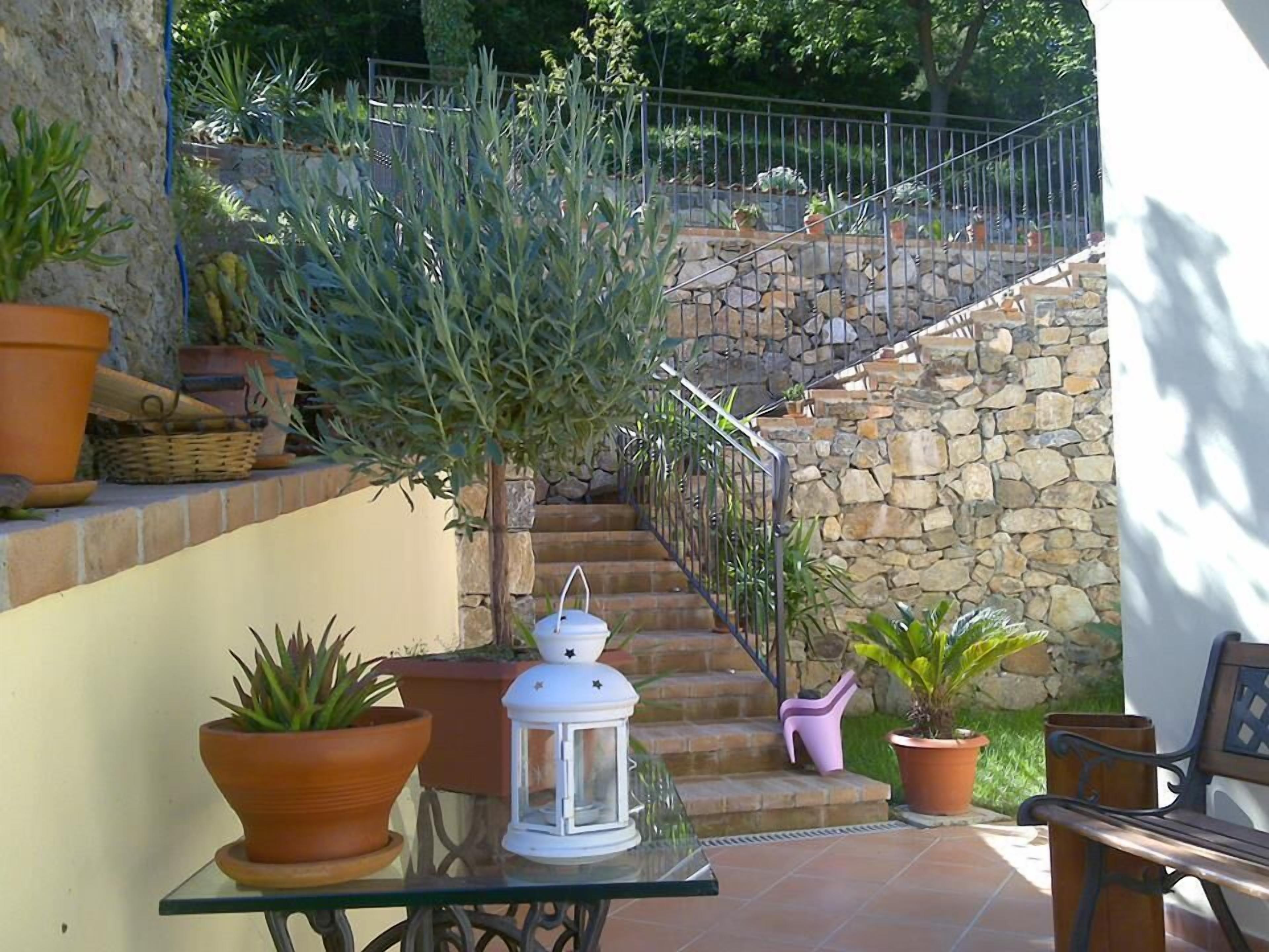 Eine Terrasse mit Glastisch, Topfpflanzen, einer weißen Laterne und einer Steintreppe.