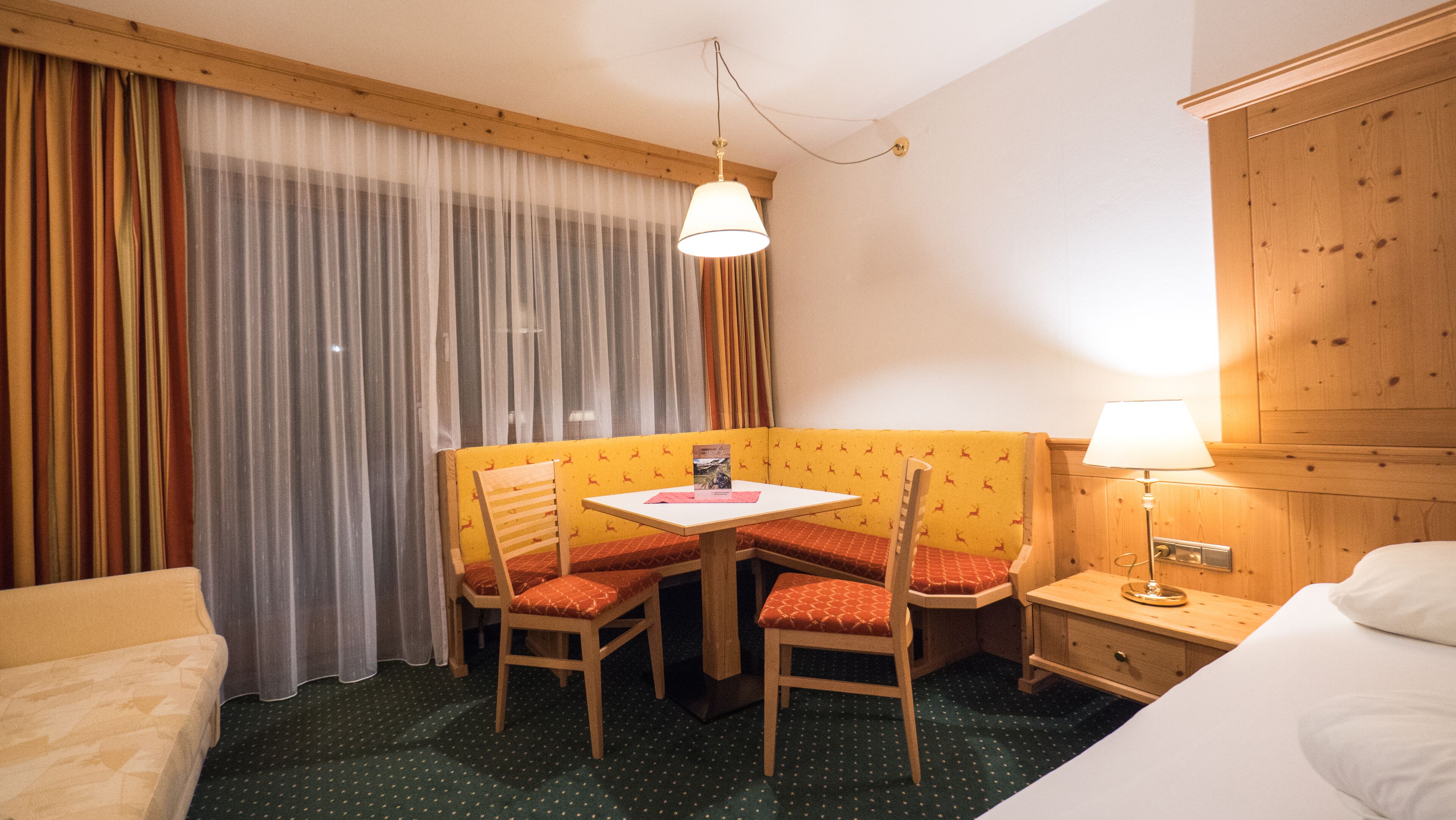 Una habitación de hotel con una cama, una pequeña mesa con sillas, una lámpara y un armario de madera.