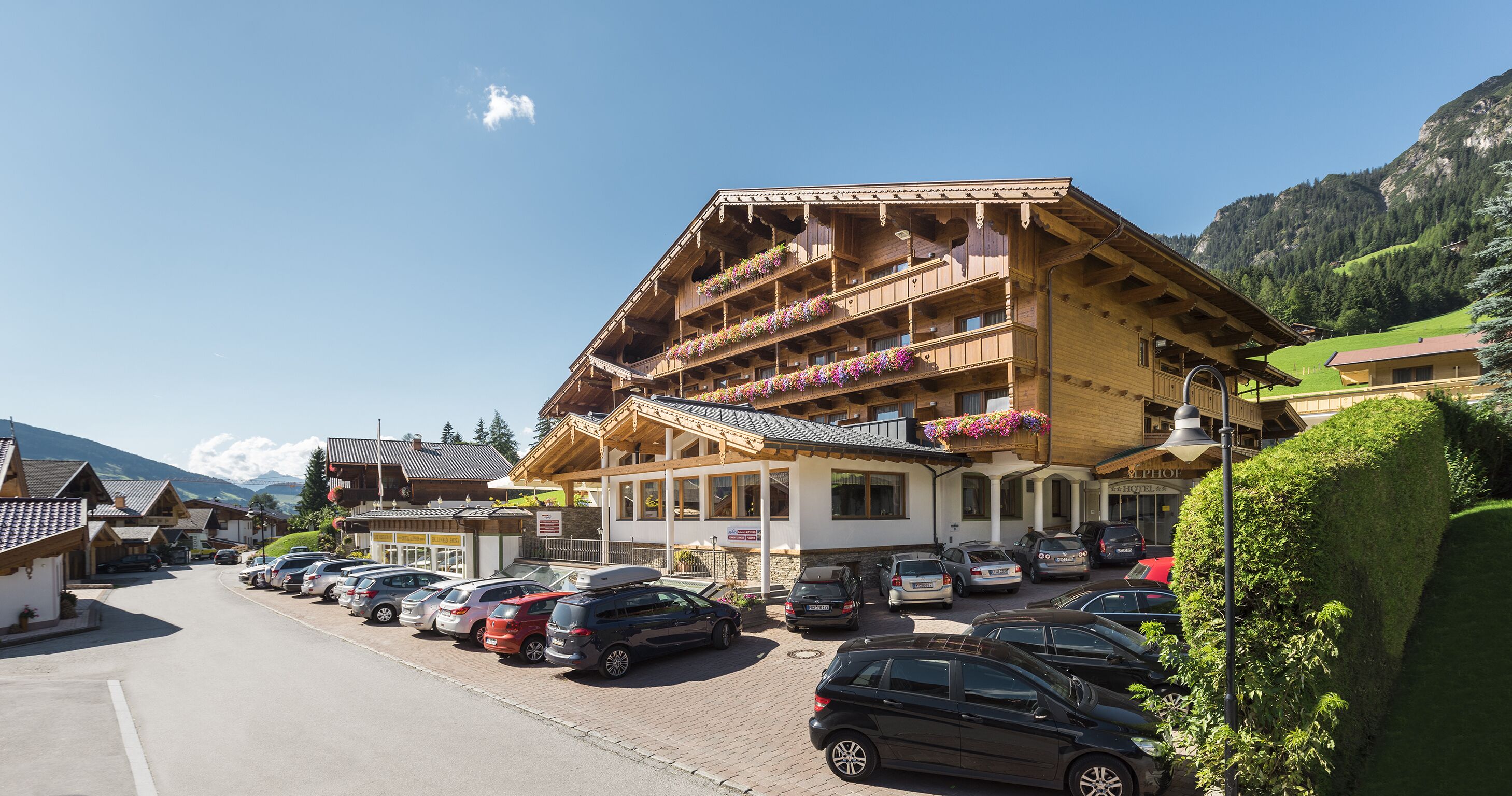 Ein traditionelles Holzhaus mit Balkonen, einem Parkplatz und einer Bergkulisse.