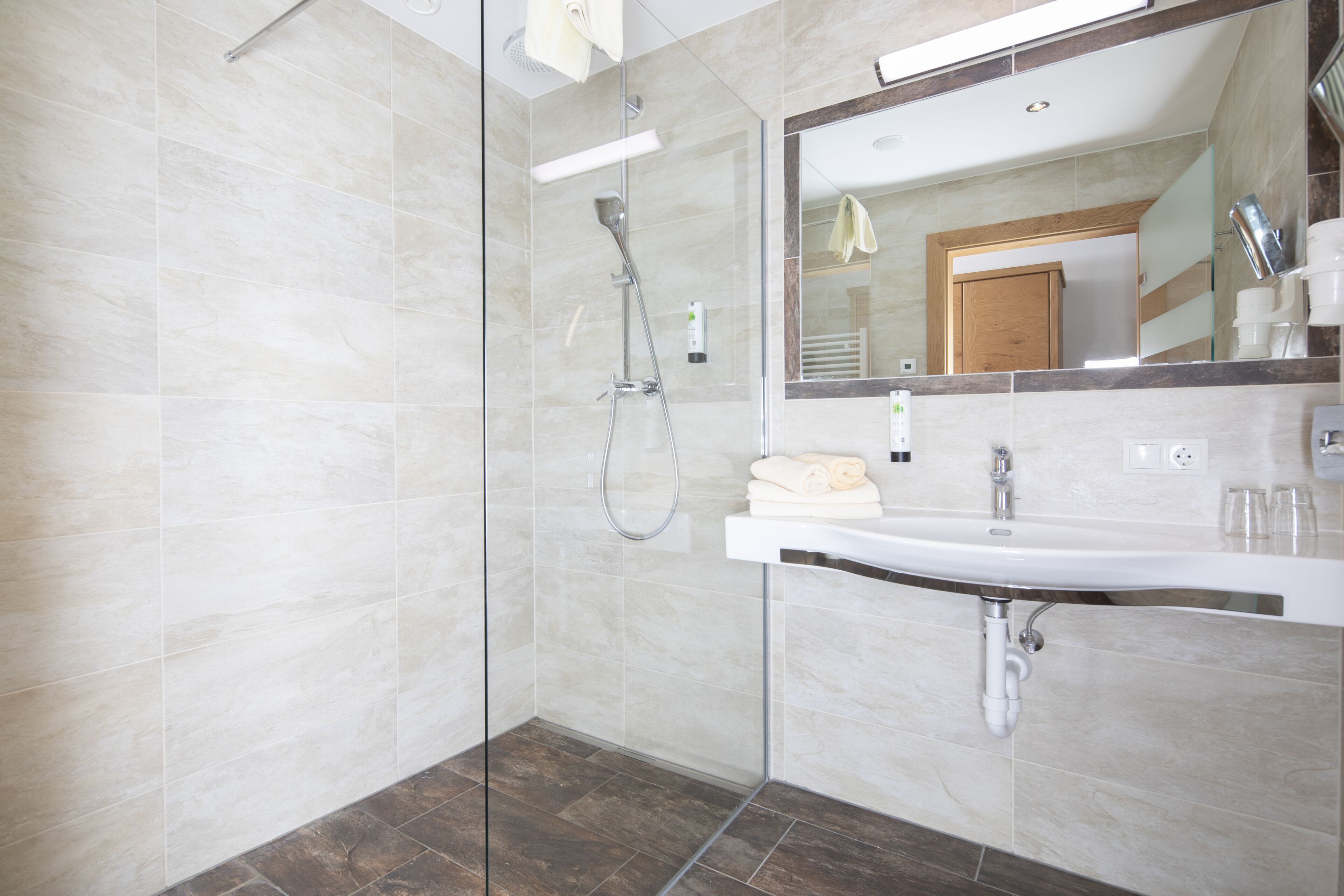 Un baño moderno con ducha de vidrio, lavamanos blanco y un espejo grande.