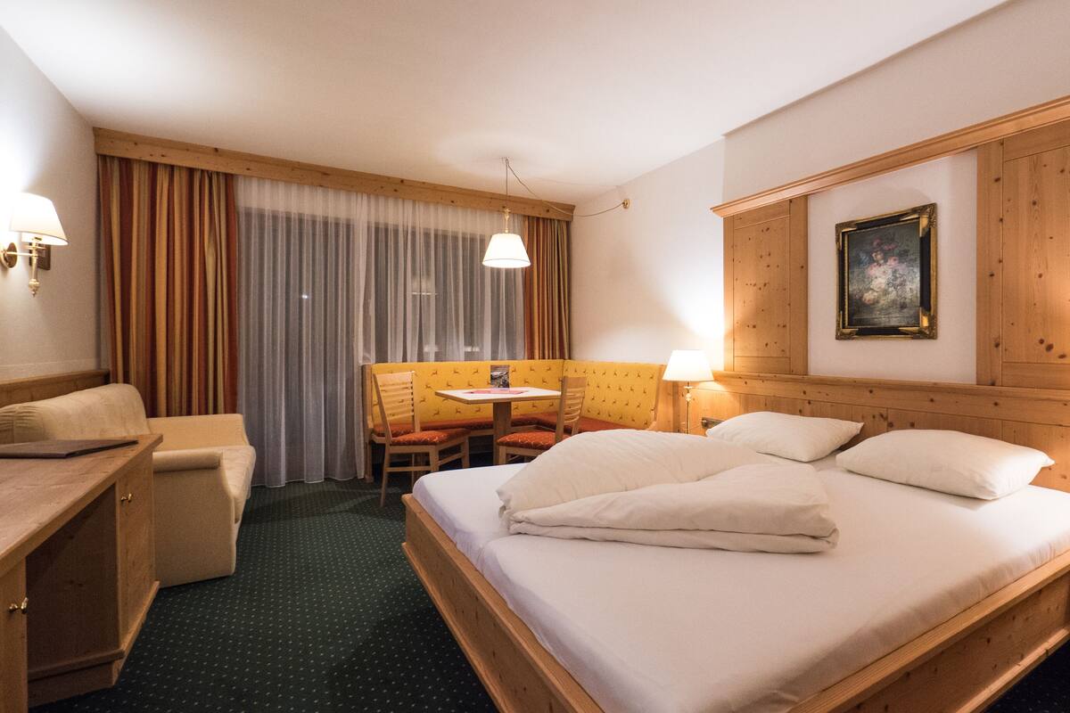 A hotel room with a large bed, a desk, a chair, and a small table.