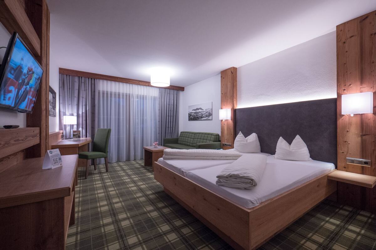 A hotel room with a large bed, a desk, a chair, a television, and a window with curtains.