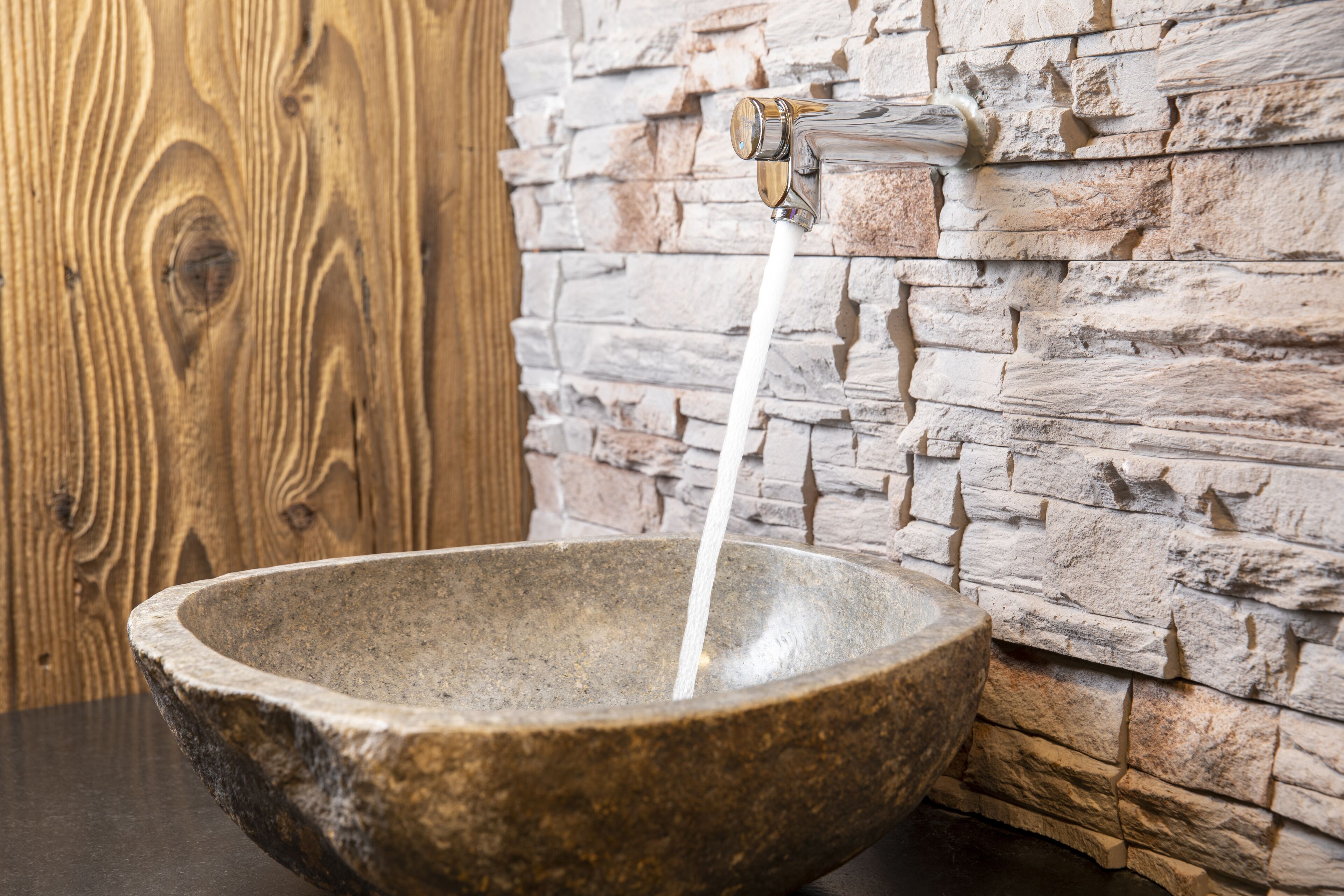 A stone basin with water flowing from a faucet against a stone wall.