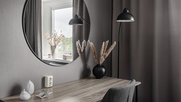 A modern room with a round mirror, a wooden desk, a vase with pampas grass, and two black floor lamps. - Stora Hotellet Markaryd (Markaryd)