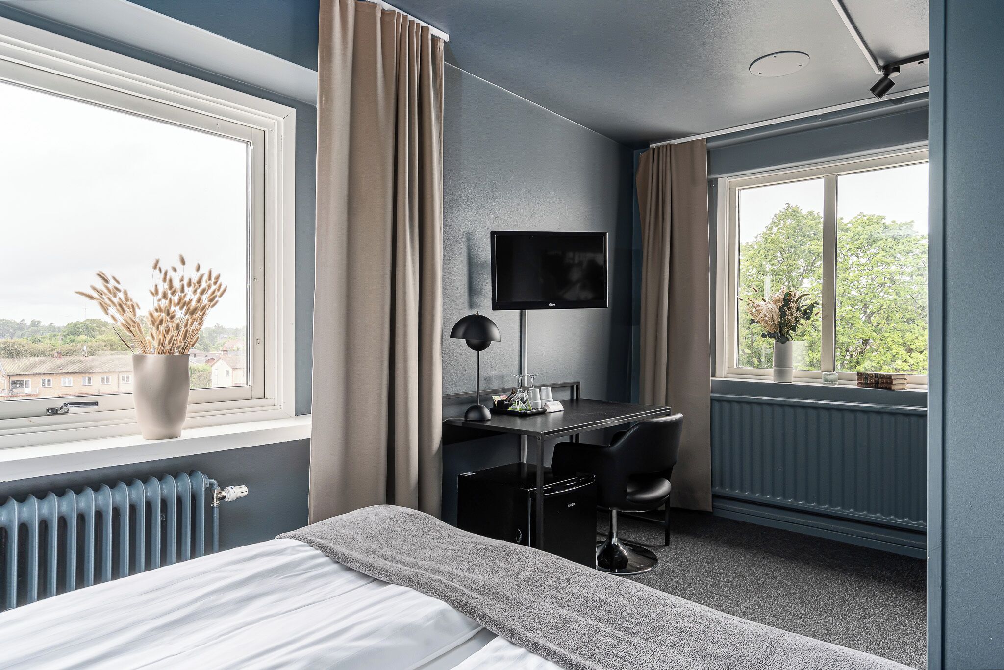 Une chambre d’hôtel avec un lit, un bureau et une chaise, une télévision et une fenêtre avec des rideaux.