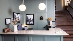A reception desk with a computer, framed pictures, and a vase with dried flowers. - Stora Hotellet Markaryd (Markaryd)