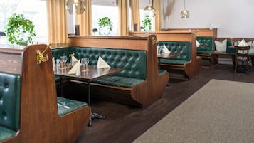 Un restaurante con cabinas tapizadas en verde, mesas de madera y lámparas colgantes.