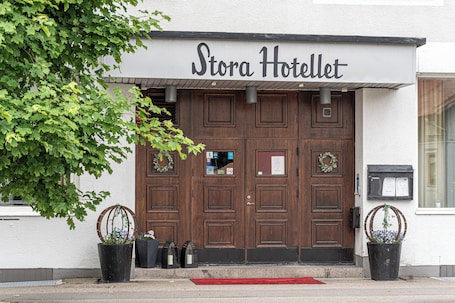 A hotel entrance with a double door, a sign above reading 'Stora Hotellet,' and two potted plants on either side.