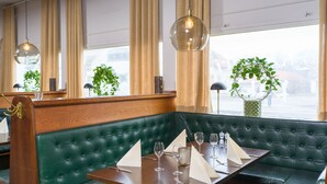 A corner booth with a wooden table set for dining, green upholstered seating, and a view of the street through large windows. - Stora Hotellet Markaryd (Markaryd)