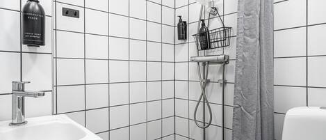 A bathroom with white tiled walls, a sink, a shower with a grey curtain, and toiletries on the wall.