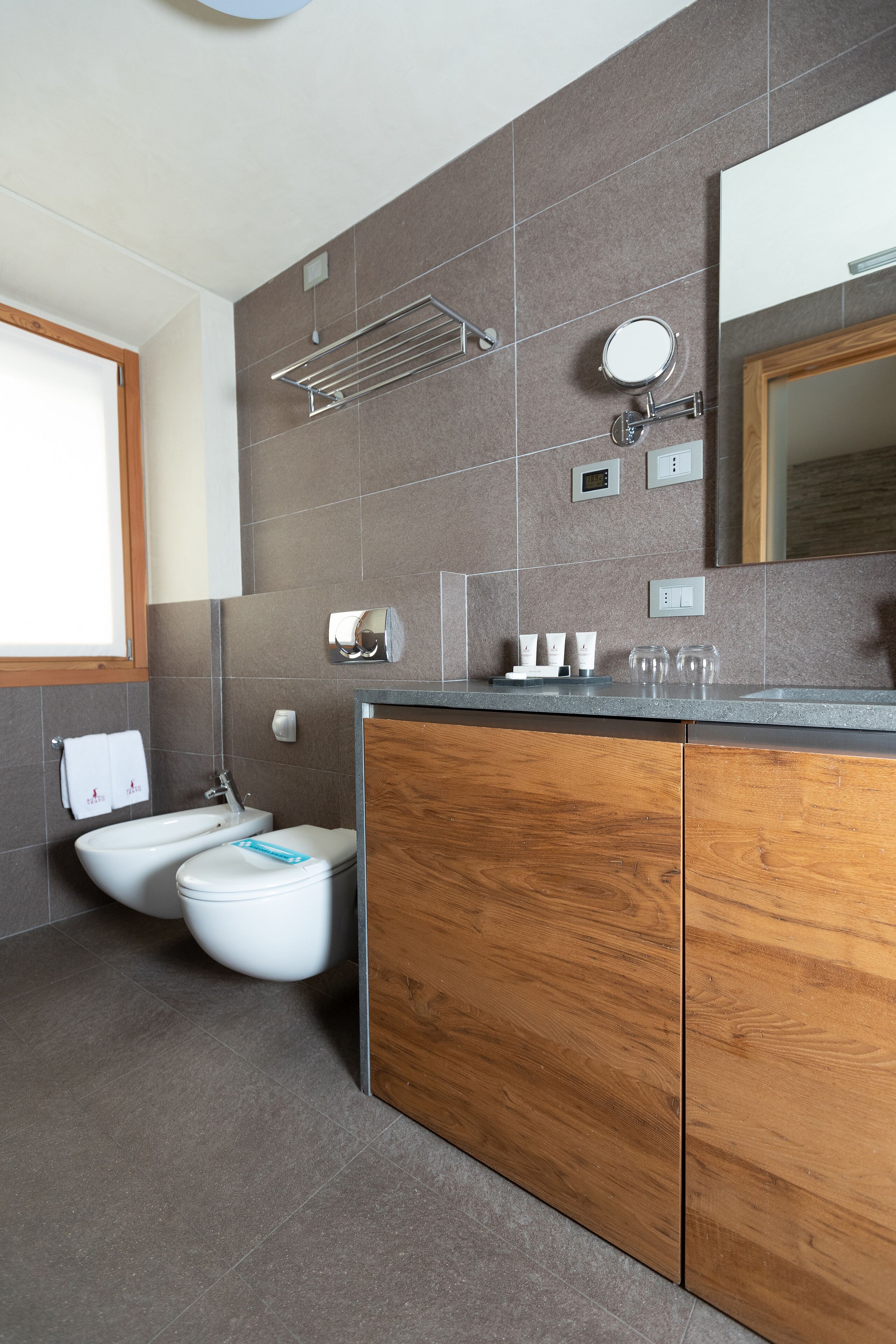 Un baño moderno con tocador de madera, un lavamanos, un inodoro y un espejo.
