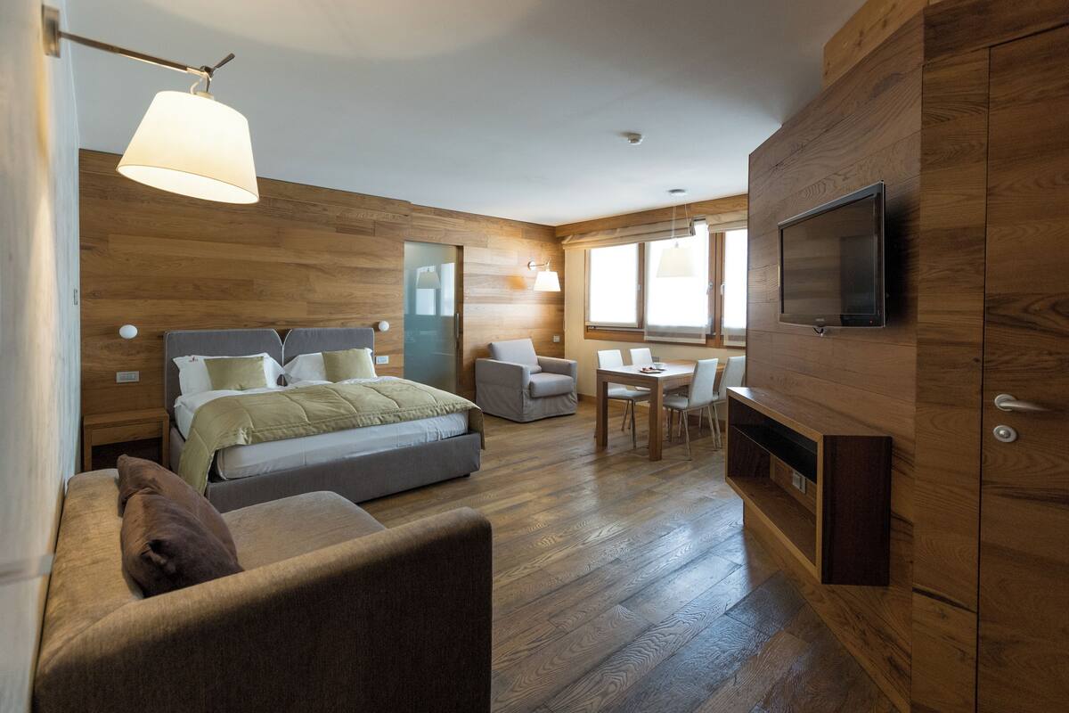Un dormitorio moderno con cama, sofá, televisor montado en la pared y una zona de comedor.