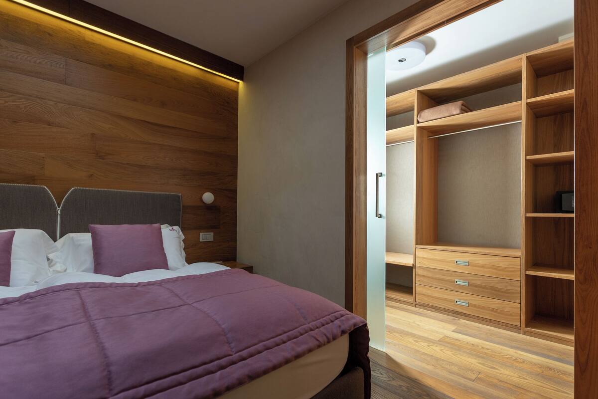 Un dormitorio moderno con cabecera de madera, cama con cubrecama morado y vestidor con estantes y cajones de madera.