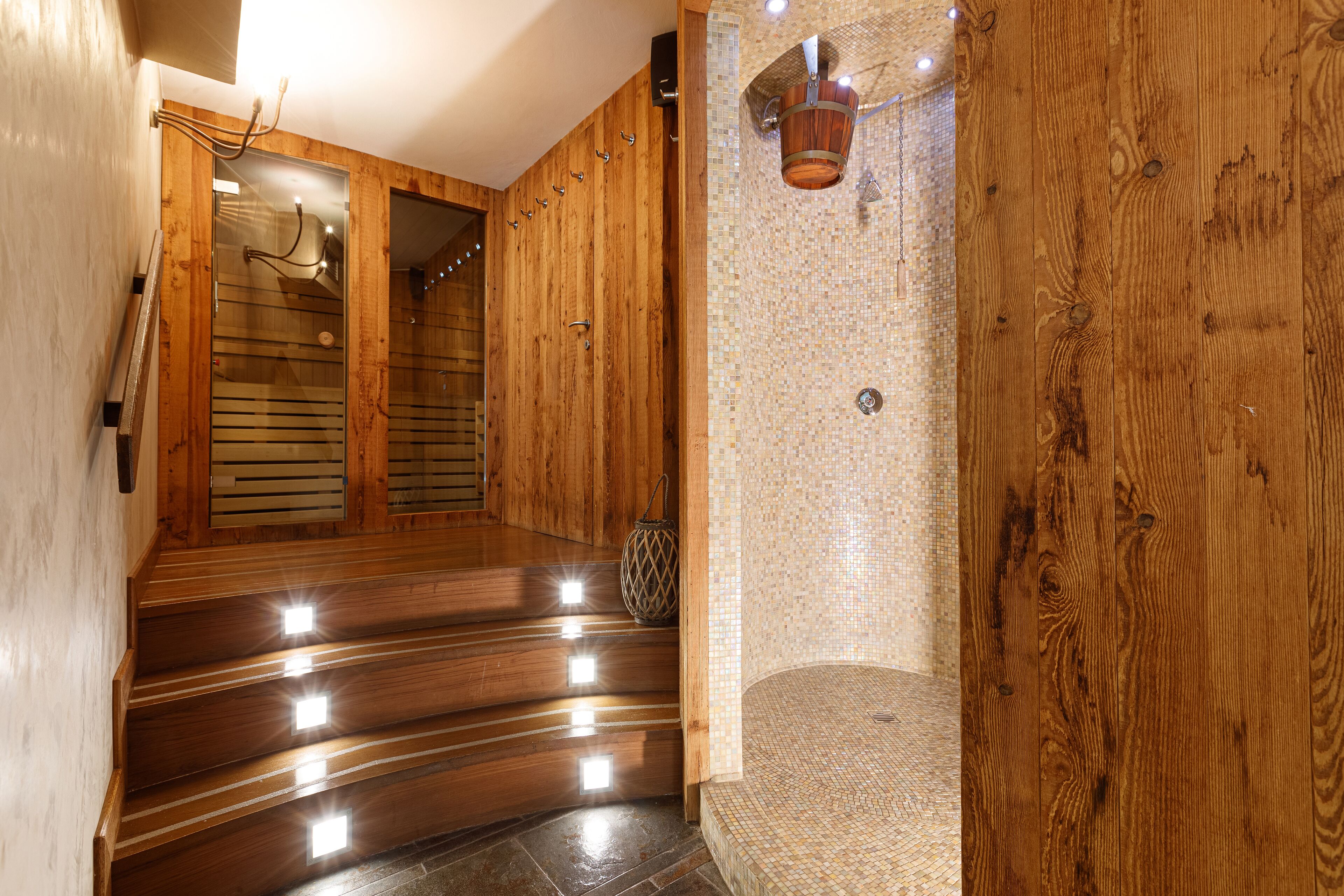 Un escalier en bois mène à un espace douche agrémenté d’un mur en mosaïque et d’un seau suspendu.