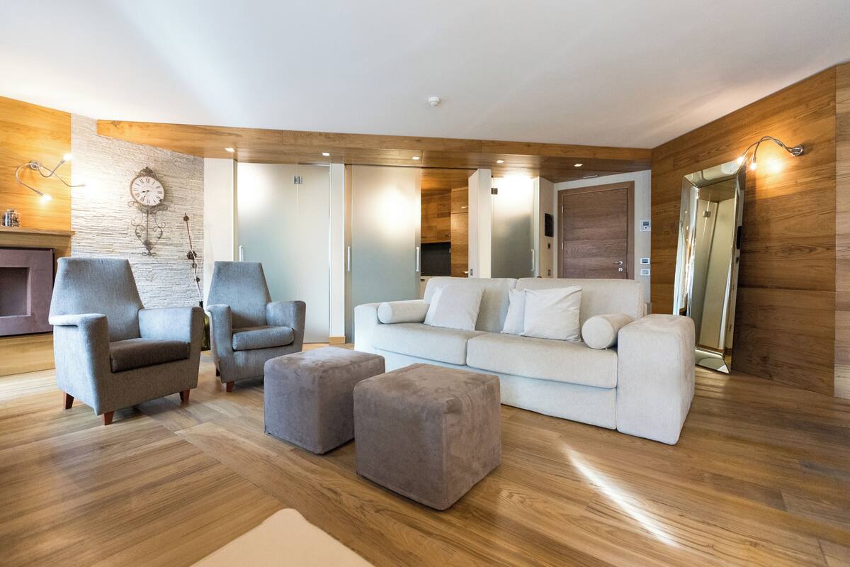 Una sala de estar moderna con piso de madera, sillones grises, un sofá blanco y otomanas grises.