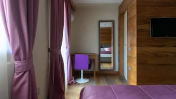 A modern hotel room with a wooden accent wall, a bed, a desk with a chair, and a television.