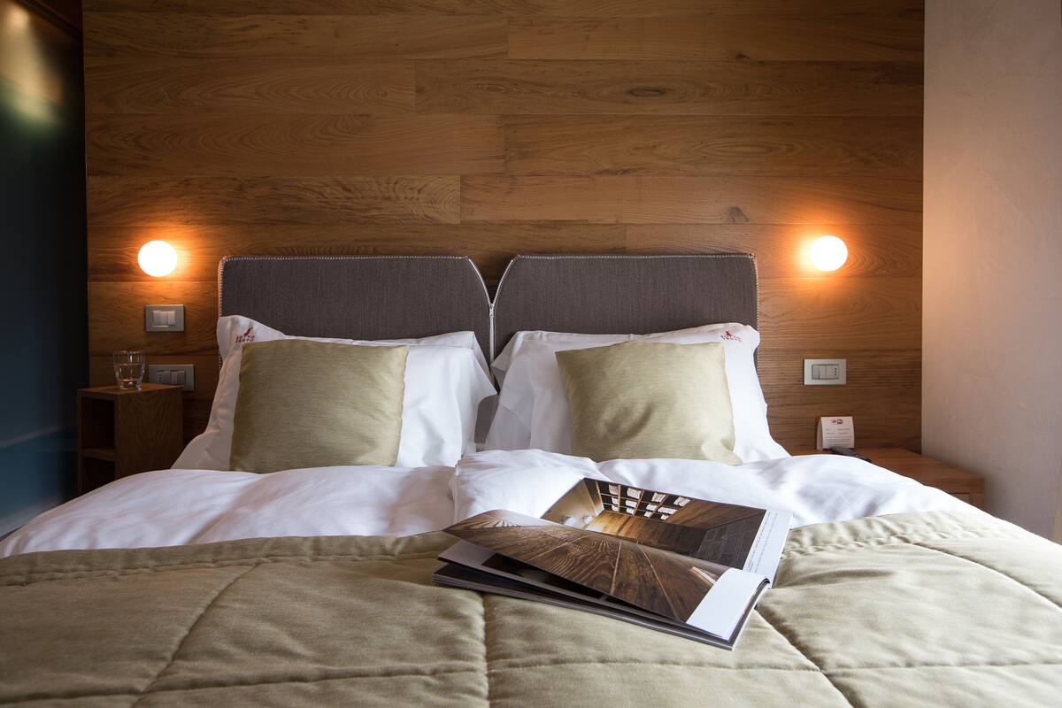 Una cama bien hecha con una colcha acolchada, dos almohadas y una revista encima.