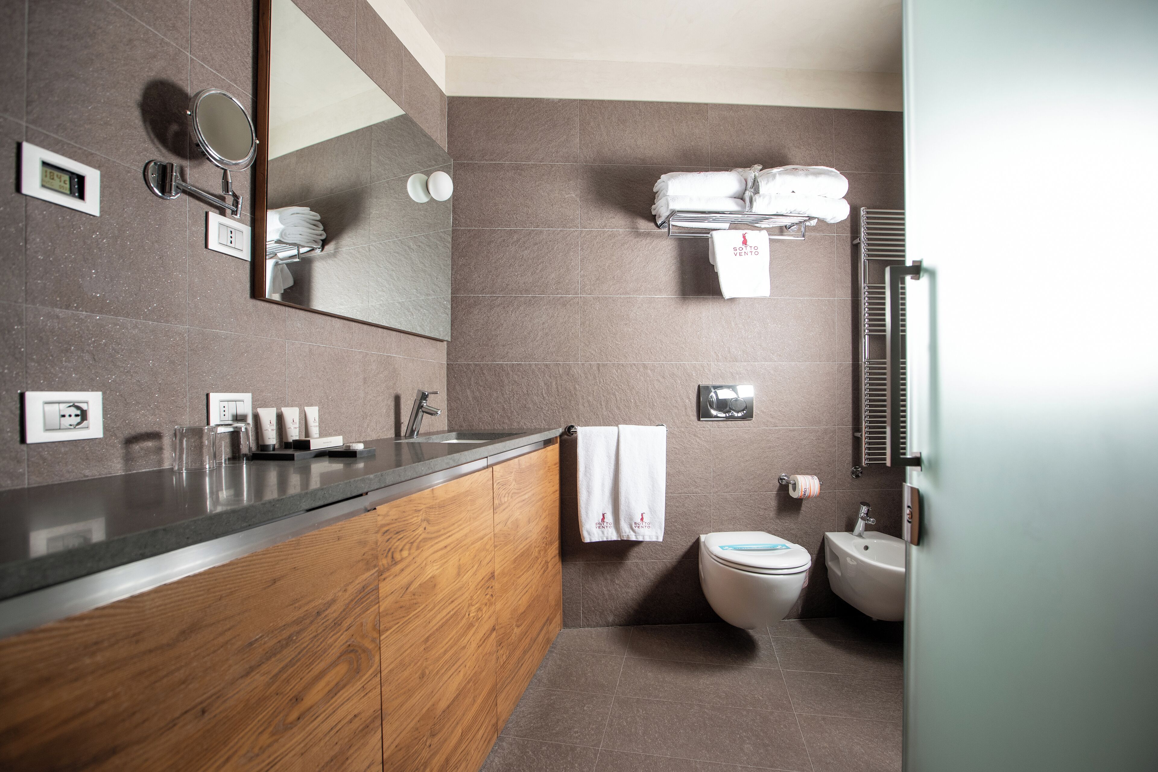 Une salle de bain moderne avec un meuble-lavabo en bois, un miroir, un porte-serviettes, des toilettes et un bidet.