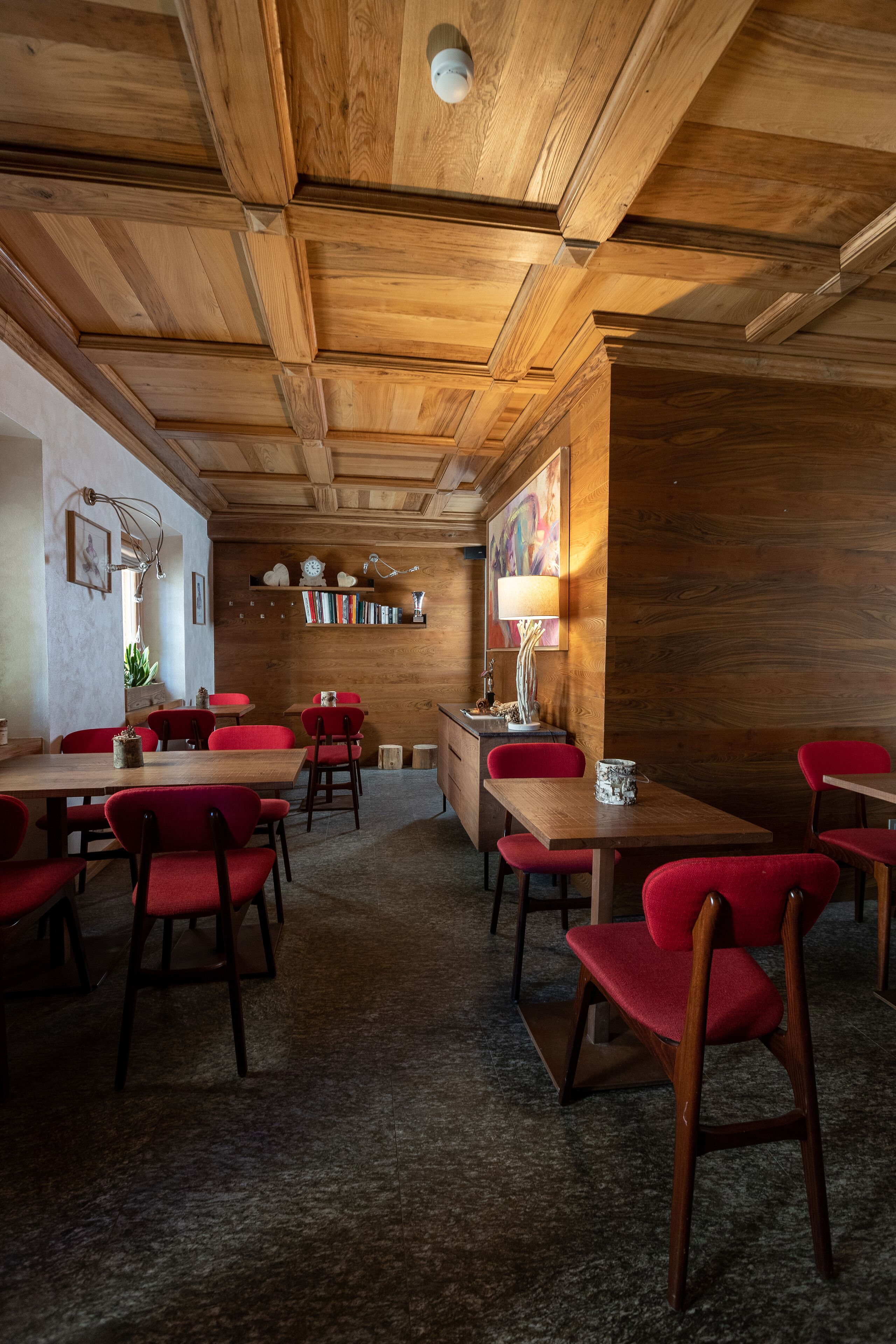Een gezellig restaurant met houten balkenplafond en rode bekleden stoelen. Tafels staan klaar voor diner.
