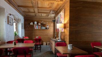 A cozy restaurant with wooden ceilings and red upholstered chairs. Tables are arranged for dining.