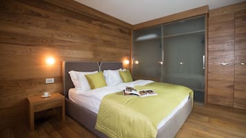 A modern bedroom with a wooden floor, a bed with a green blanket, a bedside table with a cup, and a wardrobe with a glass door.