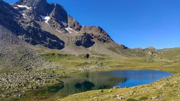 A mountainous landscape with a clear lake, rocky terrain, and a small building in the distance.