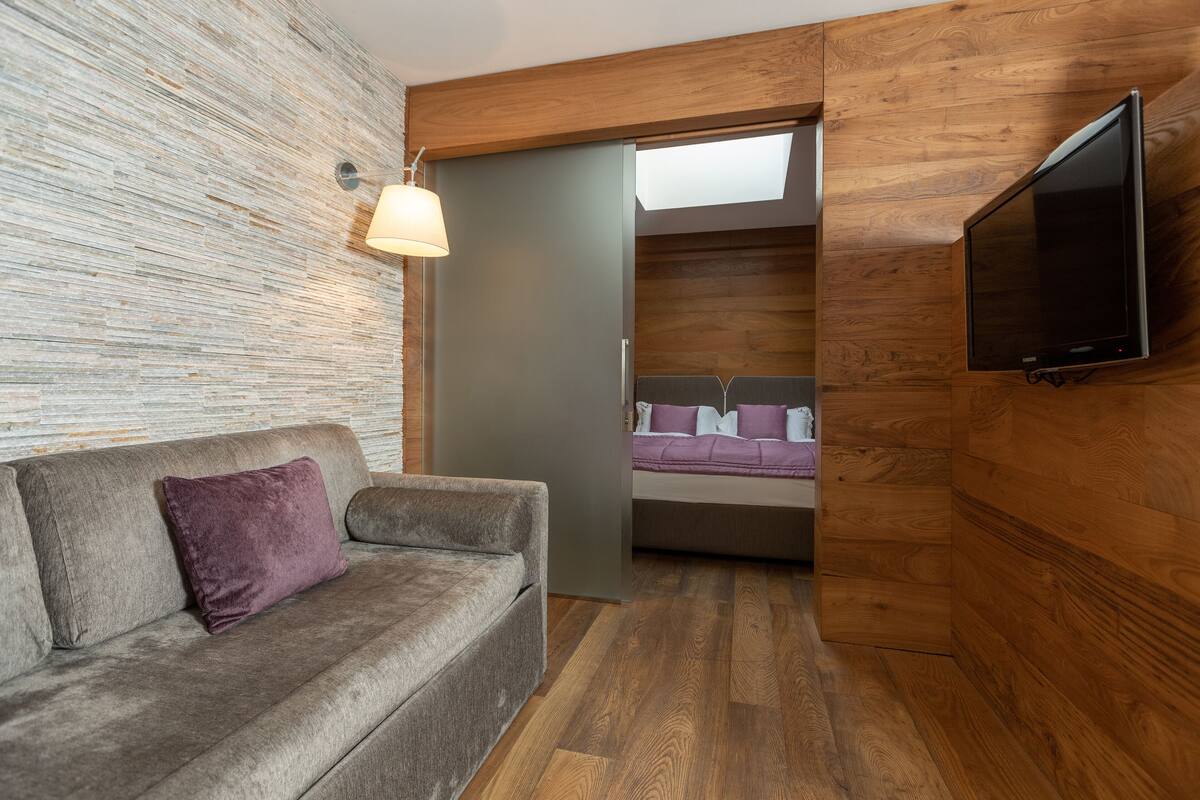 Una habitación moderna con un sofá gris, un televisor montado, suelo de madera y una pared de piedra.