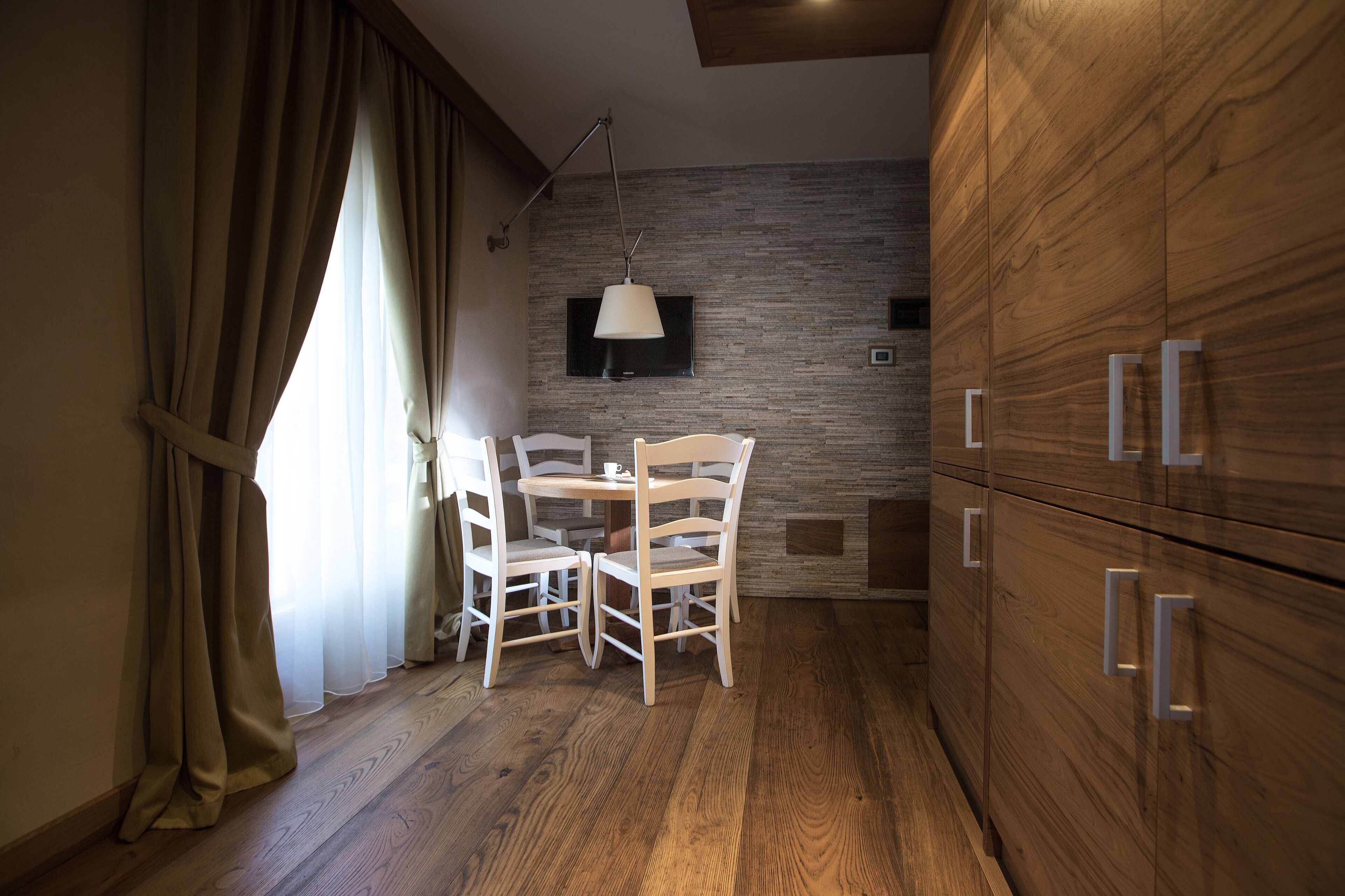 A dining area with a table and chairs, a TV mounted on the wall, and wooden cabinets.